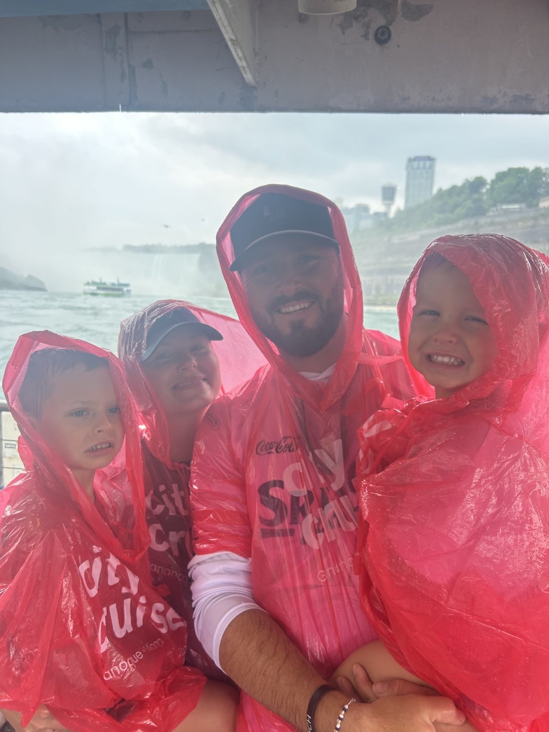 Une famille en imperméables rouges sourit à bord du bateau de Niagara City Cruises, les chutes derrière elle